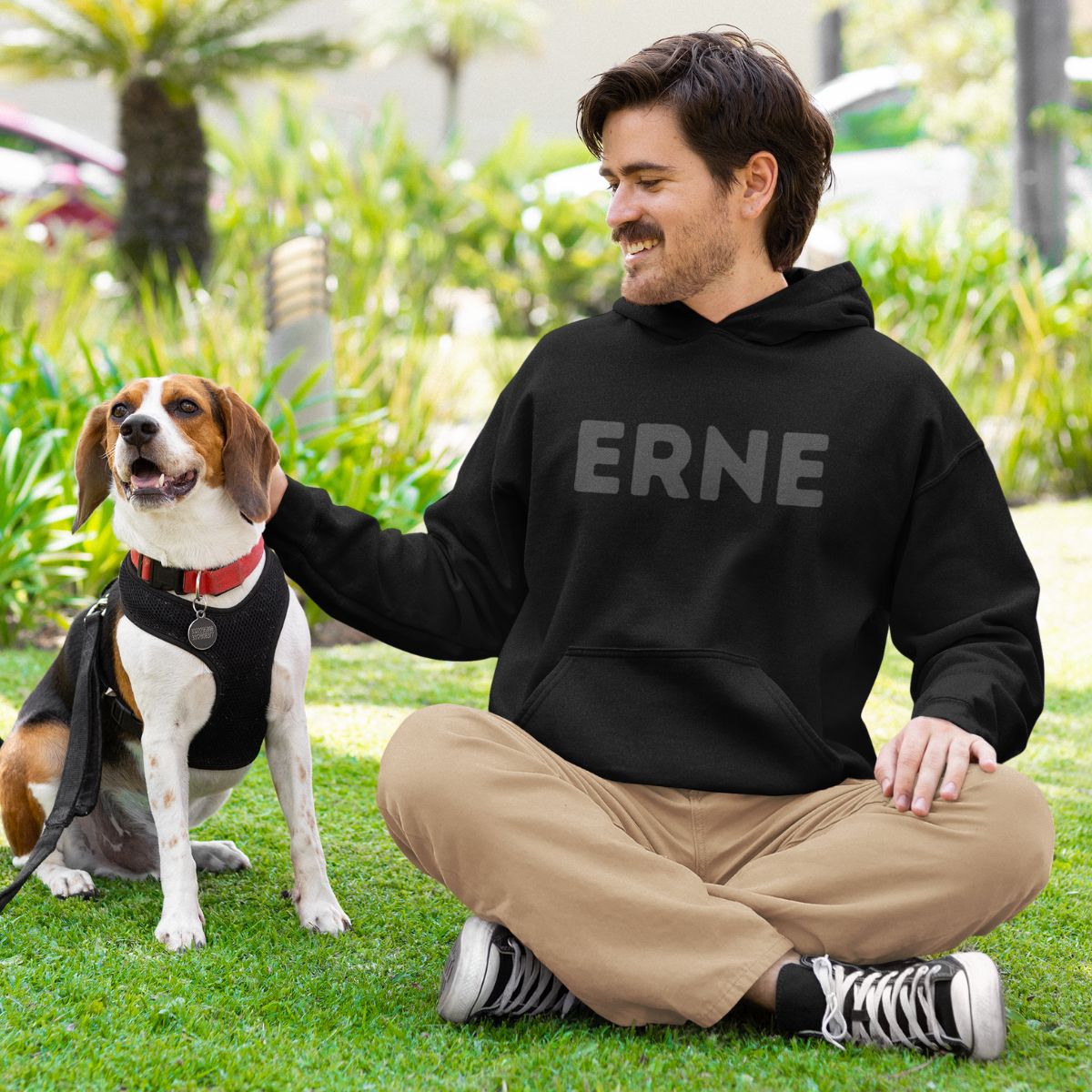 Man sitting with a dog in the park. the man is wearing a black pickleball hoodie that says Erne