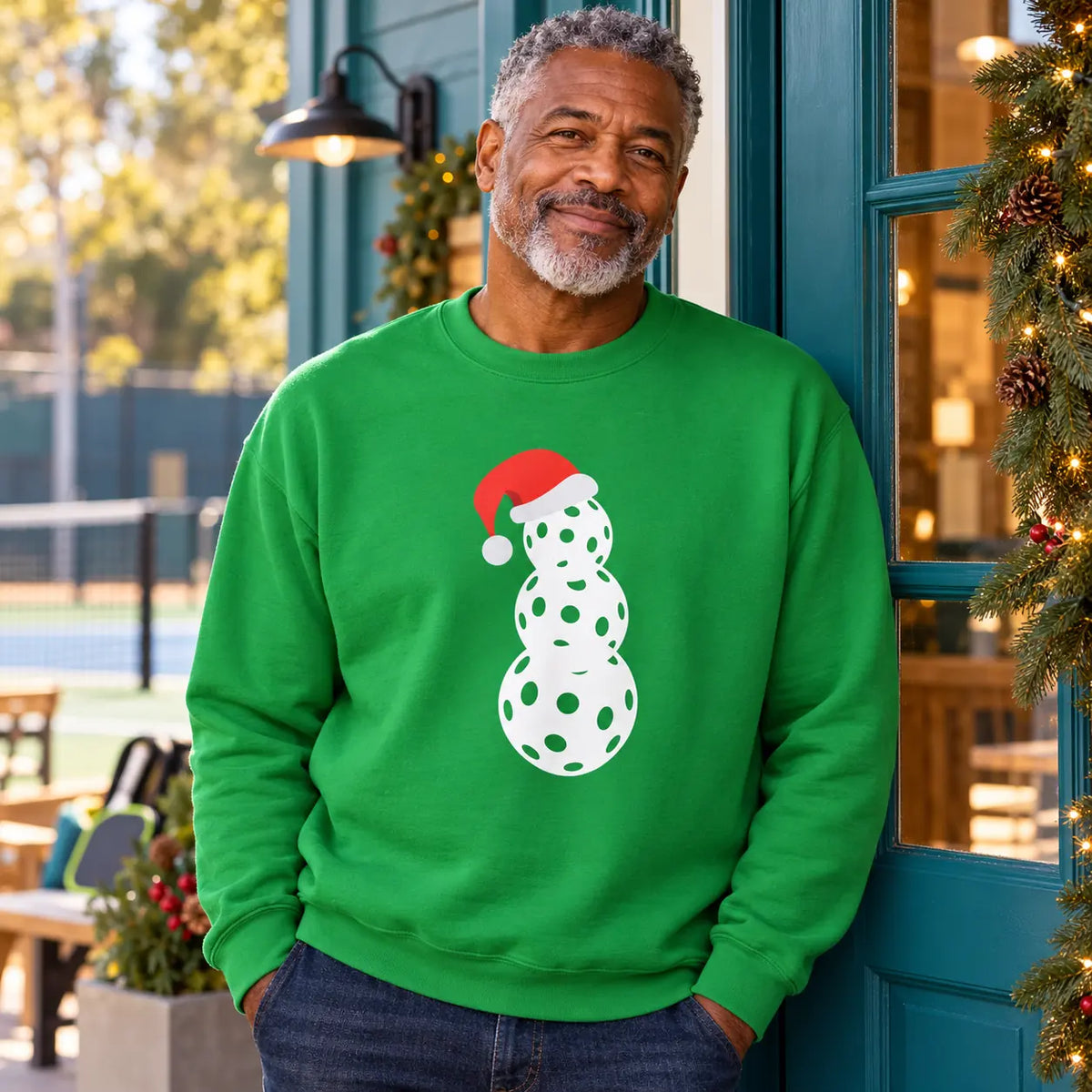 Man wearing a green pickleball snowman sweatshirt outside a clubhouse.