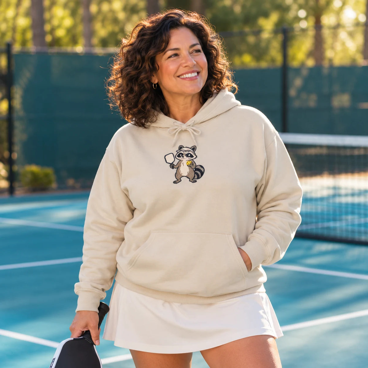 Woman wearing a sand raccoon pickleball hoodie on the court.