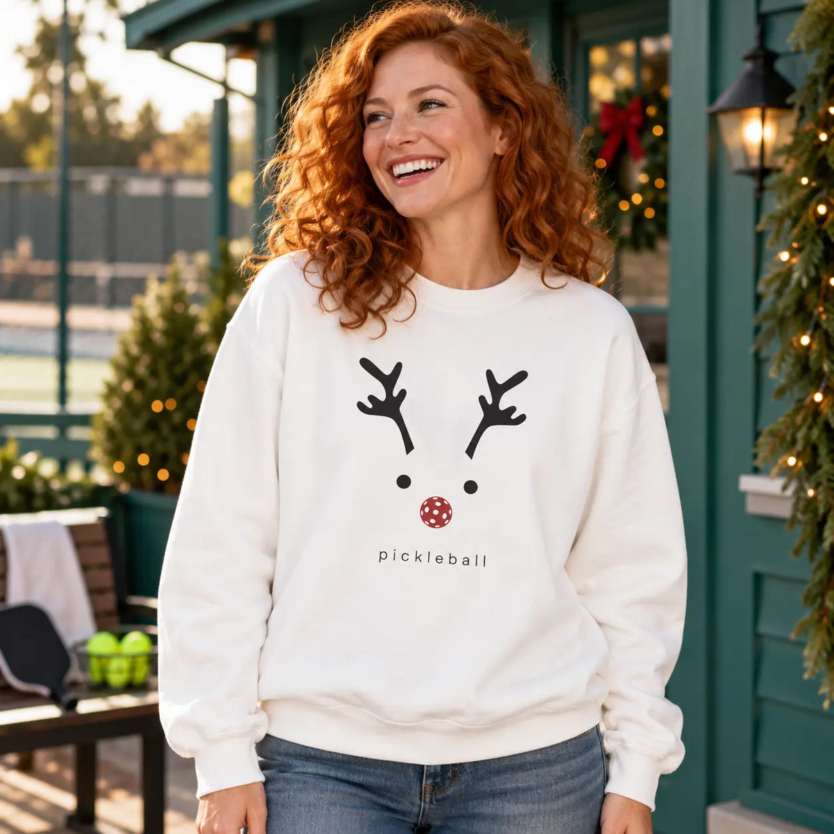 Woman wearing a white reindeer pickleball sweatshirt outside a festive clubhouse.